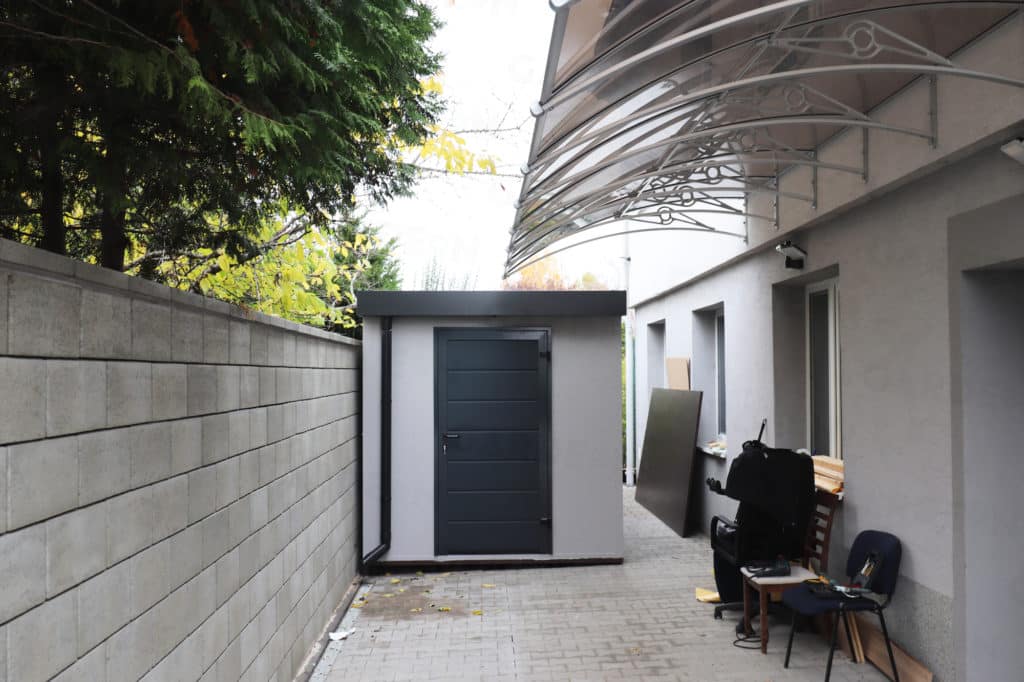 Domek ogrodowy w jasnoszarym tynku przy domu jednorodzinnym