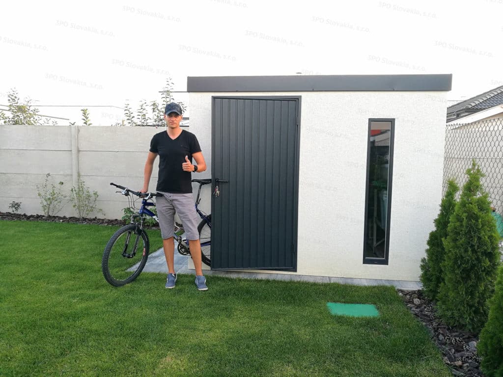 Spokojný zákazník pred montovaným záhradným domčekom GARDEON v bielej omietke