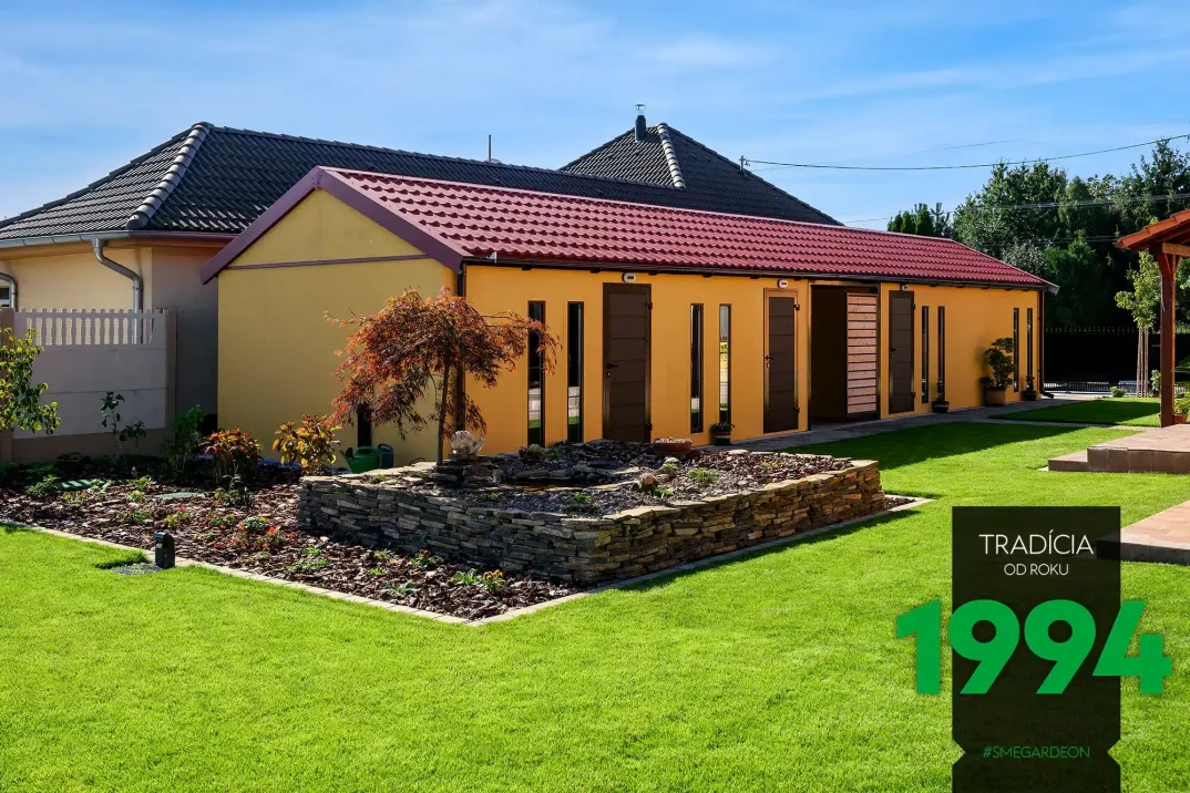 Atypická montovaná garáž ve žluté omítce s hnědými doplňky a sedlovou střechou.