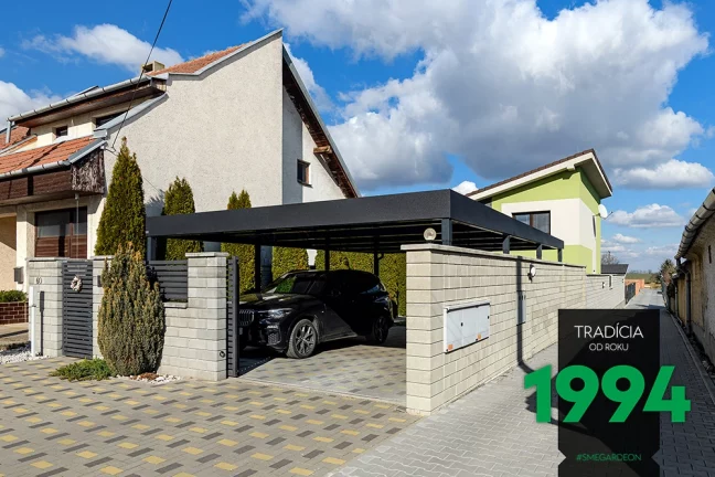 Auto pod přístřeškem za betonovým plotem