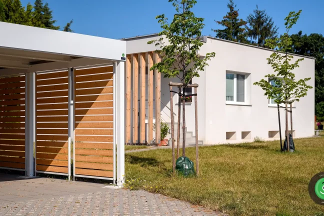 Přístřešek pro dvě auta s bílou střechou mezi stromy v zahradě