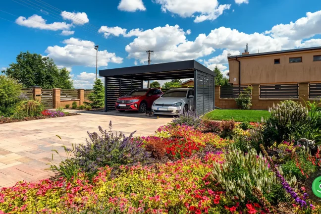 Přístřešek pro auta na zámkové dlažbě obklopený květinovou zahradou