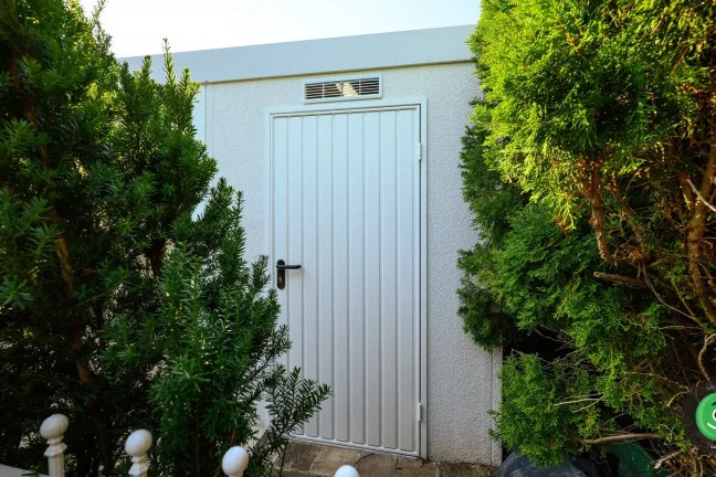 Dveře zahradního domku skryté mezi velkými zelenými stromy