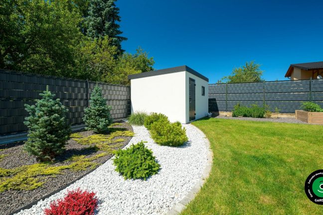 Bílý zahradní domek obklopený zelení a květinami.