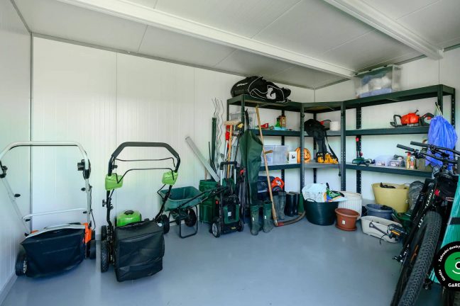 Vnitřek bílého zahradního domku s odleženými zahradními věcmi.