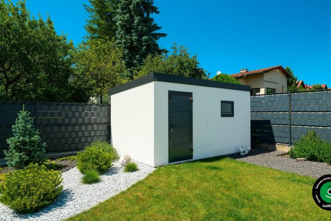 Zahradní domek v bílé, mezi trávou a stromy.