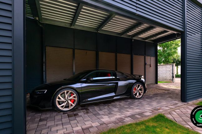 Luxusní černý sporťák zaparkovaný pod kovovým přístřeškem.