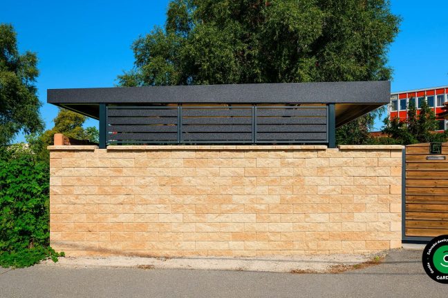 Pohled zvenčí na přístřešek ukrytý za kamennou zdí.