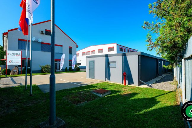 Garáže v areálu firmy s administrativní budovou v pozadí.