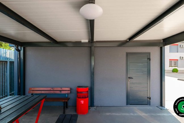 Zastřešený prostor se stolem a lavičkami u garáží.