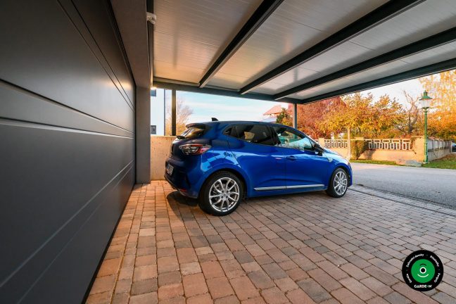 Modré auto pod přístřeškem u velké garáže