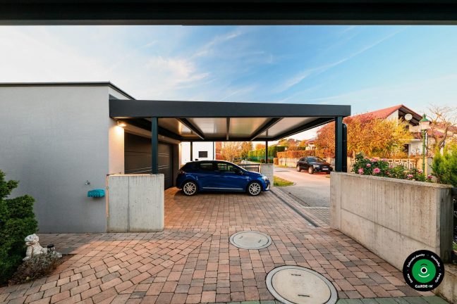 Auto pod přístřeškem u betonové stěny a zahrady