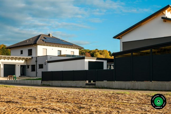 Moderní garáž u rodinného domu s tmavým plotovým oplocením